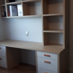 Usługi stolarsko budowlane Józef Grapa - Biurko z szufladami i nadstawką z półkami, jasne drewno, szare fronty szuflad z miedzianymi uchwytami, na półkach segregatory i teczki.