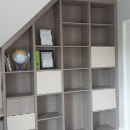 Usługi stolarsko budowlane Józef Grapa - Szara zabudowa meblowa z półkami i szafkami wnękowymi, dopasowana do skosu dachu w Zubrzycy Górnej, z dekoracjami na półkach.