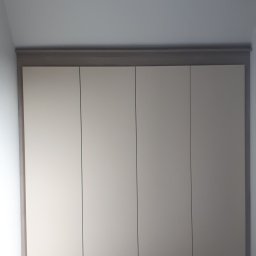 Usługi stolarsko budowlane Józef Grapa - Czterodrzwiowa szafa wnękowa z jasnymi frontami i ciemniejszym obramowaniem, wkomponowana w skos pomieszczenia.