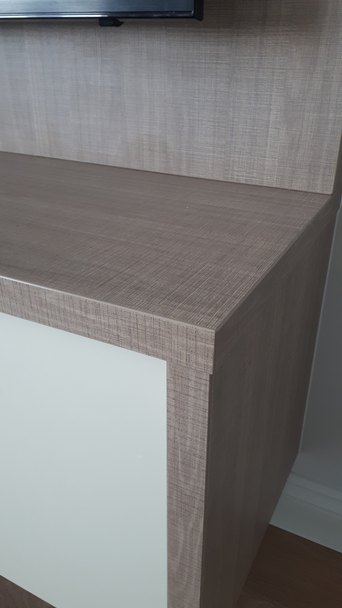 Fragment szafki RTV z blatem w odcieniach szarości i frontem w kolorze białym, widoczny fragment telewizora na górze.