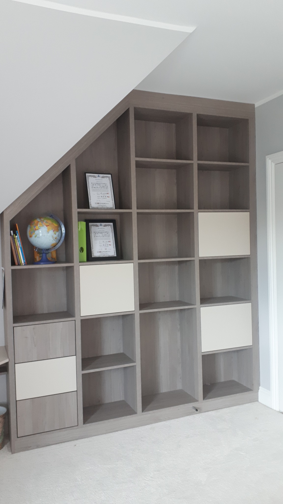 Szara zabudowa meblowa z półkami i szafkami wnękowymi, dopasowana do skosu dachu w Zubrzycy Górnej, z dekoracjami na półkach.