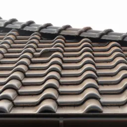 Brązowa dachówka ceramiczna o falistym wzorze, z widocznym elementem wentylacyjnym w górnej części połaci dachowej i orynnowaniem w dolnej części kadru.