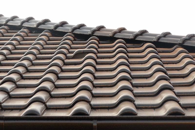 Brązowa dachówka ceramiczna o falistym wzorze, z widocznym elementem wentylacyjnym w górnej części połaci dachowej i orynnowaniem w dolnej części kadru.