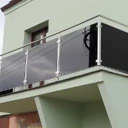Balkon z balustradą ze stali nierdzewnej z czarnymi szklanymi panelami, widoczny słup energetyczny odbijający się w szkle.