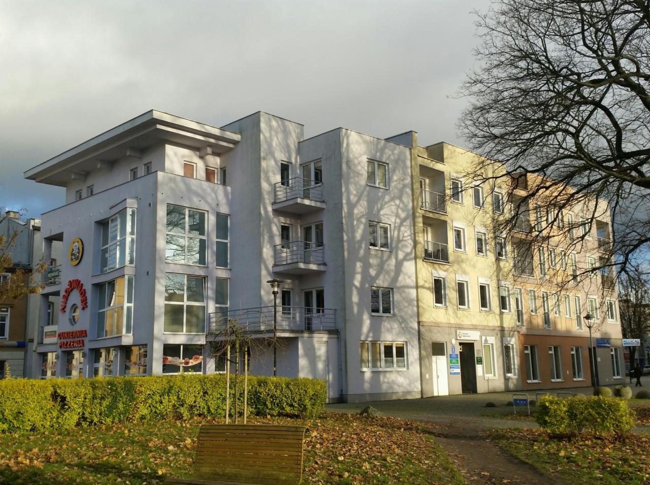 Nowoczesny budynek z biurami i lokalami usługowymi, widoczne szyldy firmowe i tablice informacyjne na elewacji.