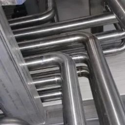 Złożona instalacja z rur stalowych o różnych średnicach, z widocznymi złączkami i mocowaniami, tworząca skomplikowany system przemysłowy. Widok z dołu.