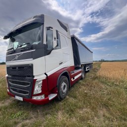 Kamień bazaltowy - transport - Nowoczesna ciężarówka Volvo FH z biało-bordową kabiną i naczepą wywrotką, zaparkowana na polnej drodze obok złotego pola zboża pod dynamicznym niebem.
