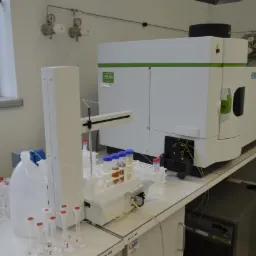 Laboratorium analityczne: automat podający próbki do spektrometru mas. Probówki, kolby i biała aparatura na stole laboratoryjnym, okno w tle.