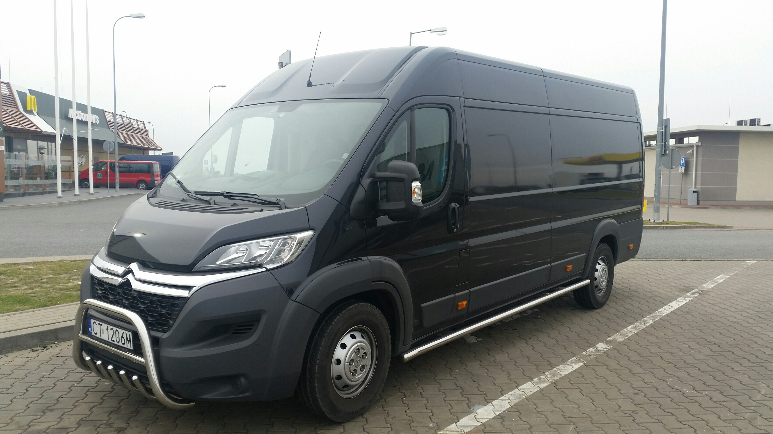 Czarny bus Citroen z chromowanym orurowaniem z przodu, zaparkowany na kostce brukowej. W tle budynek restauracji McDonald's i inne pojazdy.