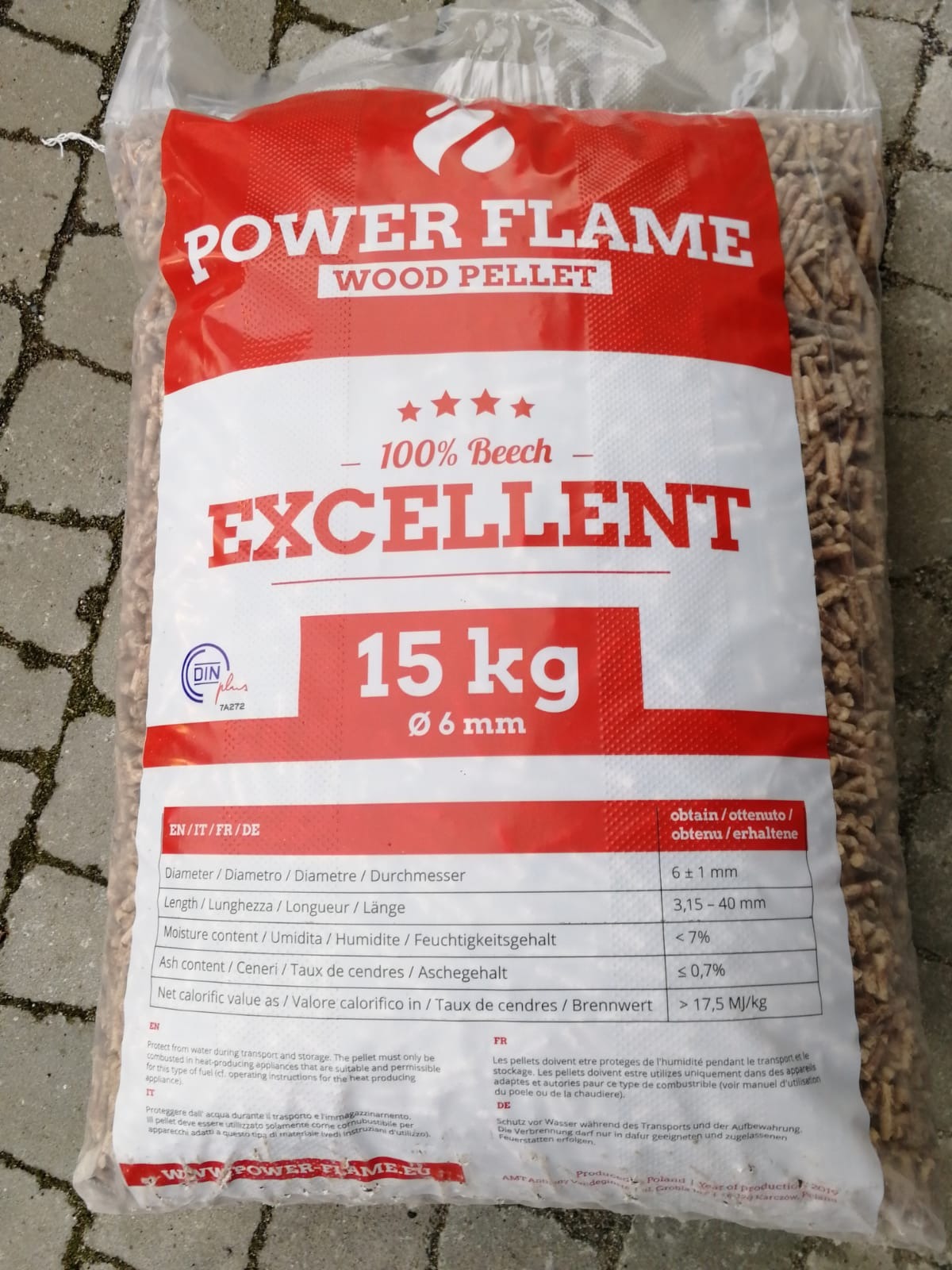 Worek z pelletem drzewnym marki Power Flame, 15 kg, z informacjami o parametrach i certyfikacie DIN Plus, leżący na brukowanej powierzchni.