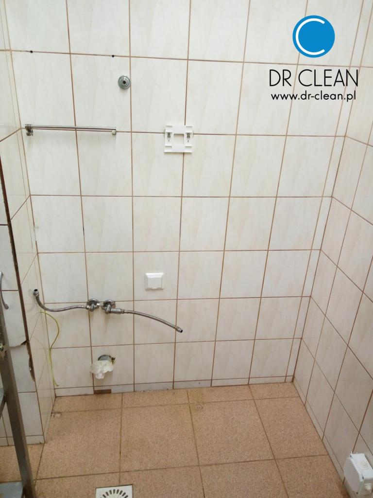 Łazienka w trakcie sprzątania po remoncie:  białe płytki, widoczne przyłącza hydrauliczne,  częściowo widoczna drabina. Logo firmy sprzątającej w prawym górnym rogu.