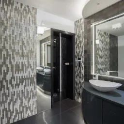 Nowoczesna łazienka z mozaiką w odcieniach szarości, podświetlanym lustrem i umywalką nablatową w kształcie łzy.