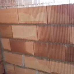 Wewnętrzny narożnik ściany z bloków ceramicznych, widoczne spoiny zaprawy, lekko wilgotna powierzchnia bloków.