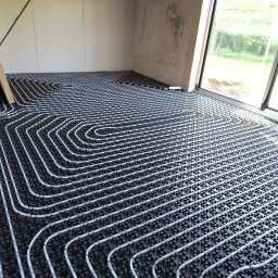 ProEnergy - Rozłożona instalacja ogrzewania podłogowego w surowym pomieszczeniu, widoczne białe rurki na czarnej macie montażowej, przygotowane do zalania wylewką.