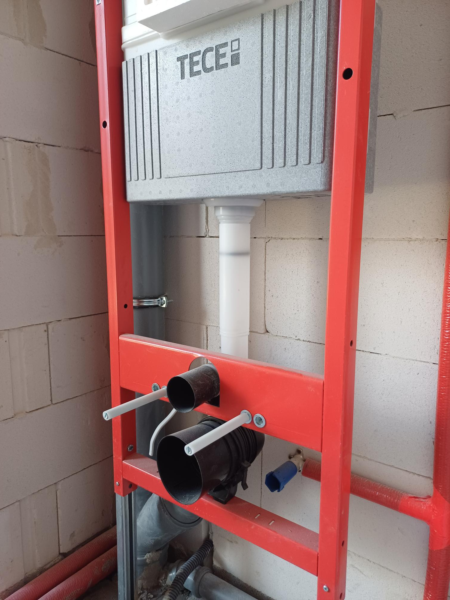 Stelaż podtynkowy WC marki TECE zamontowany przy ścianie z betonu komórkowego, widoczne rury doprowadzające wodę i odpływ ścieków.