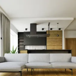 Nowoczesne wnętrze: szara sofa narożna na tle otwartej kuchni z drewnianymi frontami i czarnym okapem. Duże okno z zasłonami dopełnia całość.