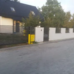 Nowoczesne ogrodzenie metalowe z poziomymi przęsłami i białą podmurówką, widoczna skrzynka gazowa w kolorze żółtym.