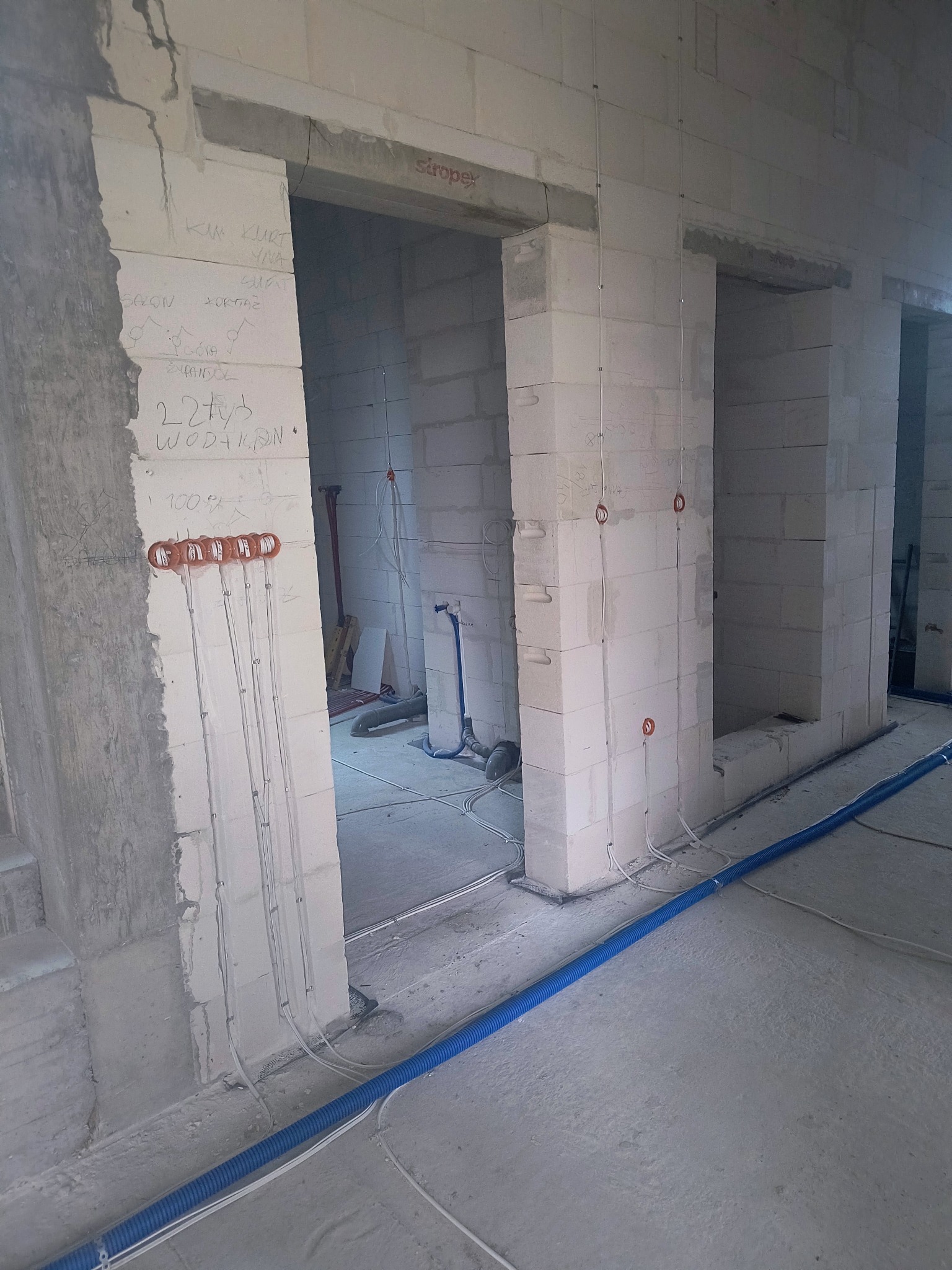 Surowy stan: przewody elektryczne w ścianie z bloczków, kable w peszlu na podłodze, przygotowane otwory na gniazdka. Instalacja elektryczna w trakcie realizacji.