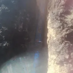 Wykop z ułożonymi niebieskimi rurami, widoczne ślady po wykopie w ziemi i częściowo zalane wodą.