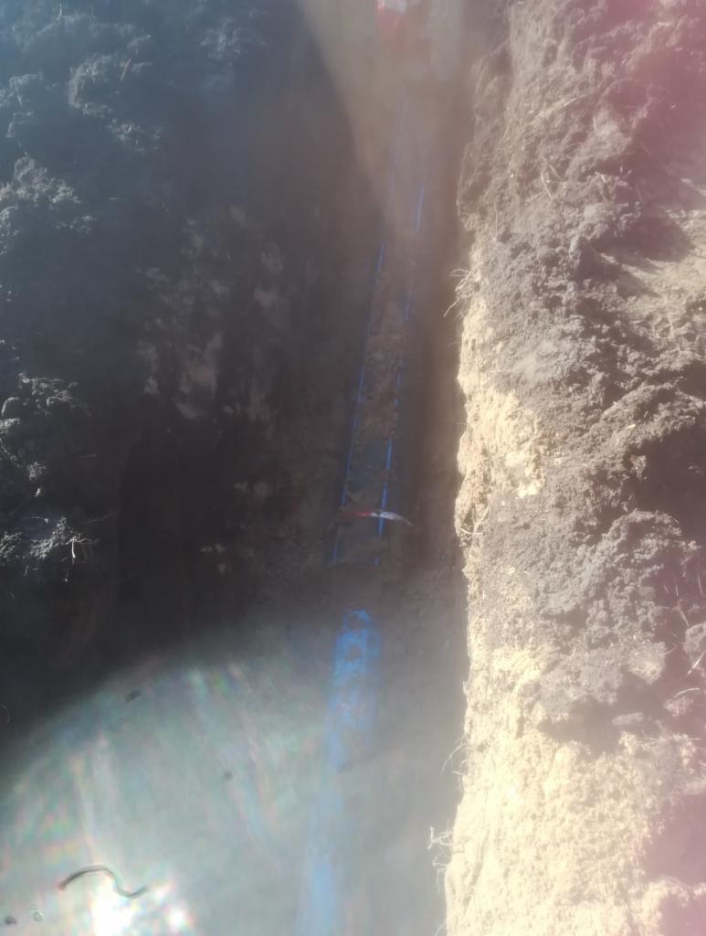 Wykop z ułożonymi niebieskimi rurami, widoczne ślady po wykopie w ziemi i częściowo zalane wodą.