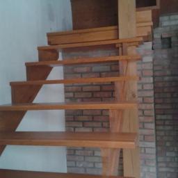 FHU Jarko - Drewniane schody bez poręczy, z widoczną konstrukcją wspornikową i ceglanym tłem, oświetlone z góry.