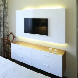 Nowoczesny salon z białymi meblami na tle ściany z podświetleniem LED. Widoczny telewizor i dekoracje. Minimalistyczny design wnętrza.