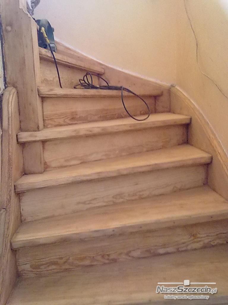 Drewniane schody w trakcie renowacji, widoczna szlifierka na górnym stopniu i kabel zasilający. Schody o jasnym odcieniu drewna, z zaokrąglonym stopniem na dole.