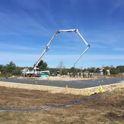 Wylewanie fundament&oacute;w domu jednorodzinnego z użyciem pompy do betonu; widoczni pracownicy budowlani i elementy szalunku.