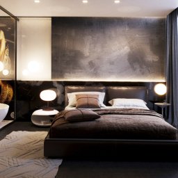 ARCHIBRANZA RAFAŁ ALEKSANDROWICZ - Nowoczesna sypialnia z łazienką oddzieloną szklaną ścianą z grafiką, ciemna kolorystyka, marmurowe wykończenia, lampy kuliste i brązowa pościel na niskim łóżku.