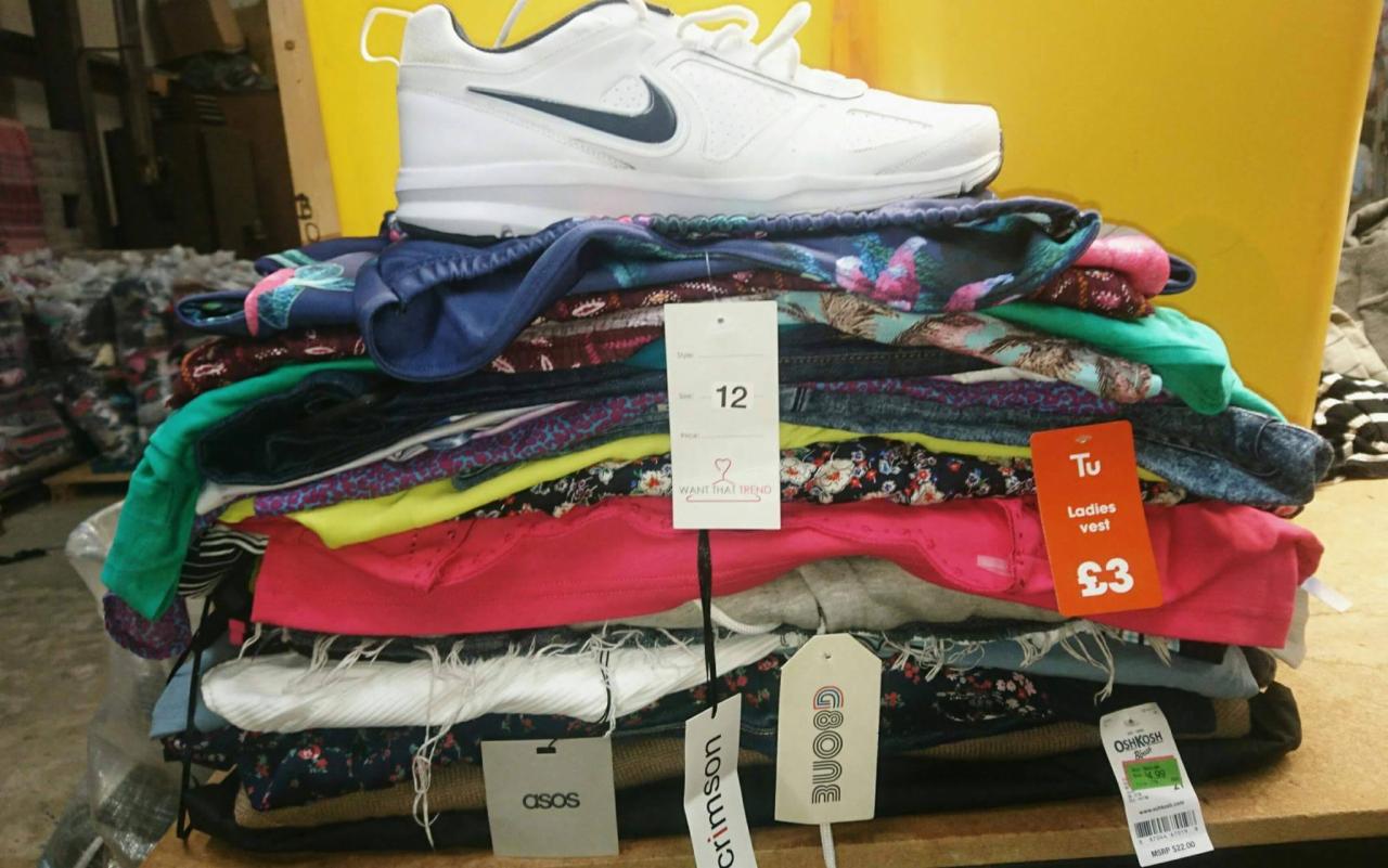 Stos ubrań z metkami różnych marek, w tym ASOS i OshKosh, zwieńczony białym butem sportowym Nike.