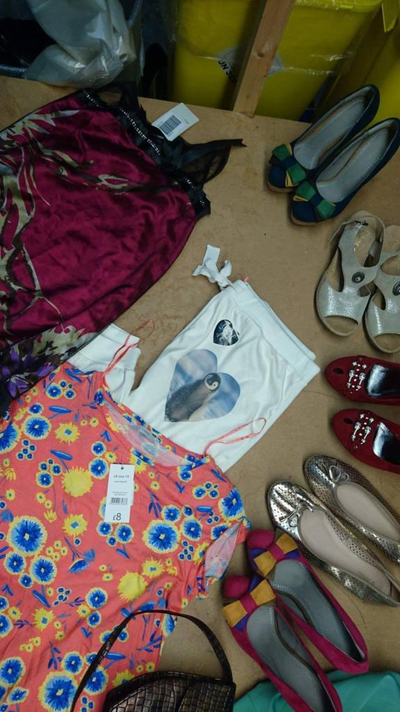Różnorodny asortyment ubrań i butów: bluzka w kwiaty z metką, satynowa koszula nocna, białe spodnie z nadrukiem pingwina w sercu, baleriny w różnych kolorach i fakturach, oraz torebka z plecionki.