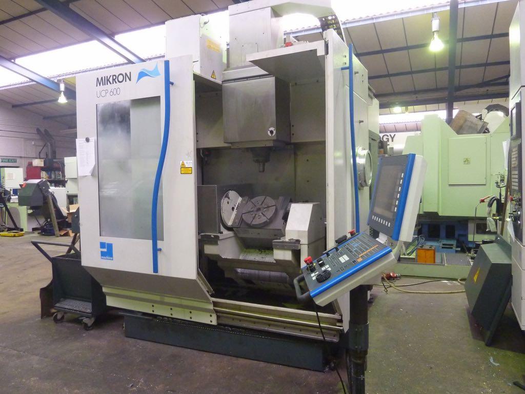 Precyzyjna frezarka CNC Mikron UCP 600 z panelem sterowania, widoczna w hali produkcyjnej. Oświetlenie sufitowe, inne maszyny w tle.