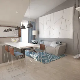 Wnętrze mieszkania z aneksem kuchennym, białym stołem barowym i wiszącymi lampami. W tle szara sofa, biała grafika na ścianie i schody linowe.