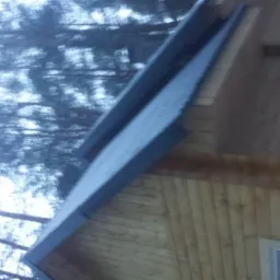 Fragment dachu z drewnianą elewacją, widoczny z dołu, na tle zamazanych drzew.