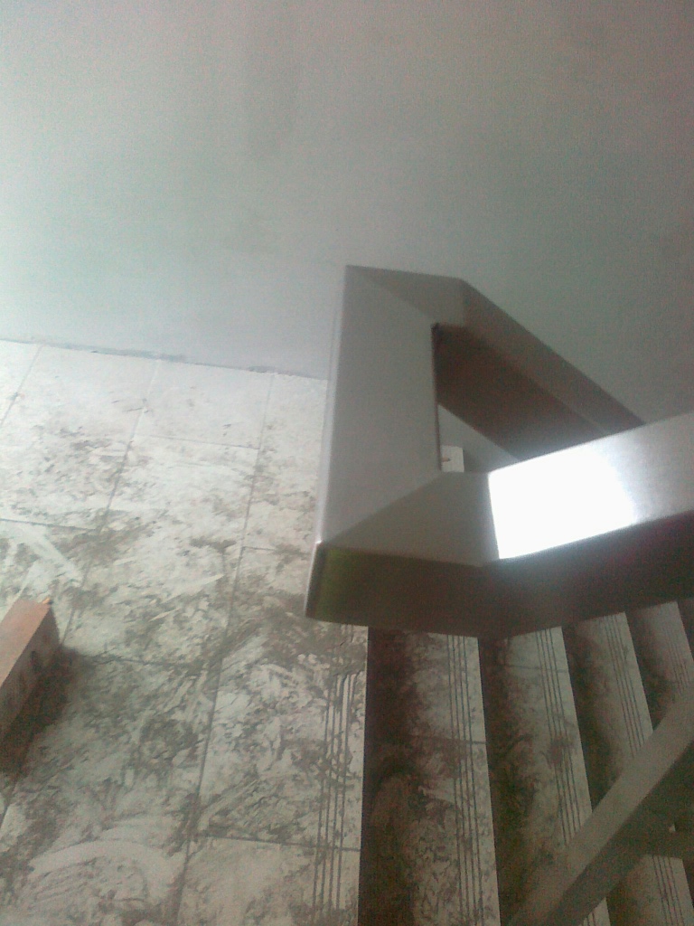 Wnętrze z fragmentem schodów wykończonych płytkami imitującymi marmur i z metalową balustradą. Widok z dołu, w tle biały sufit.