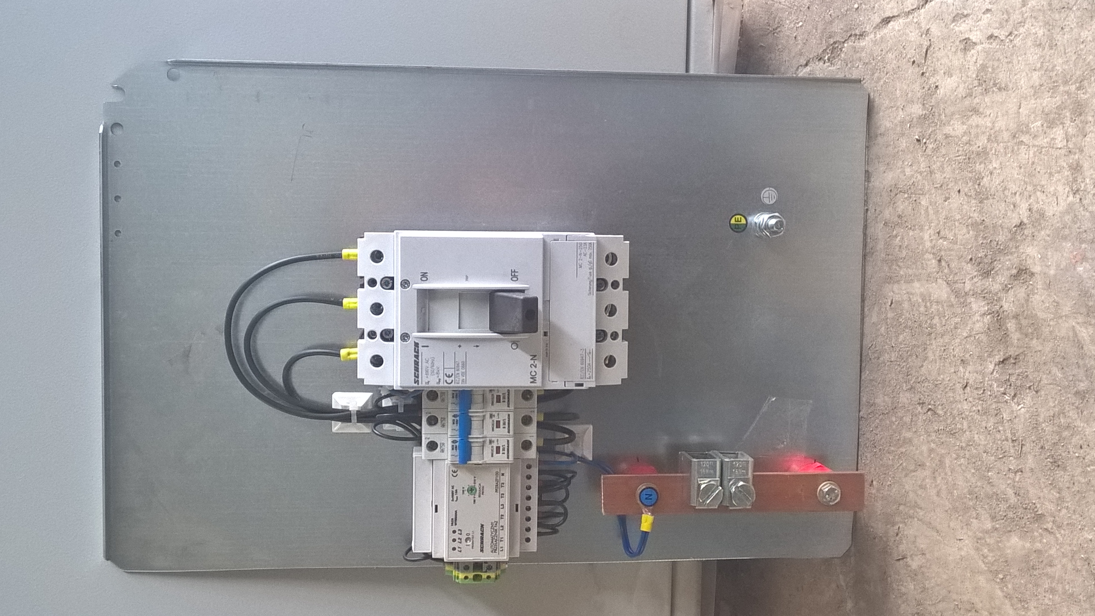 Rozdzielnica elektryczna z wyłącznikiem i zabezpieczeniami, widok z góry. Elementy połączone przewodami. Widoczna listwa zaciskowa. Metalowa obudowa.