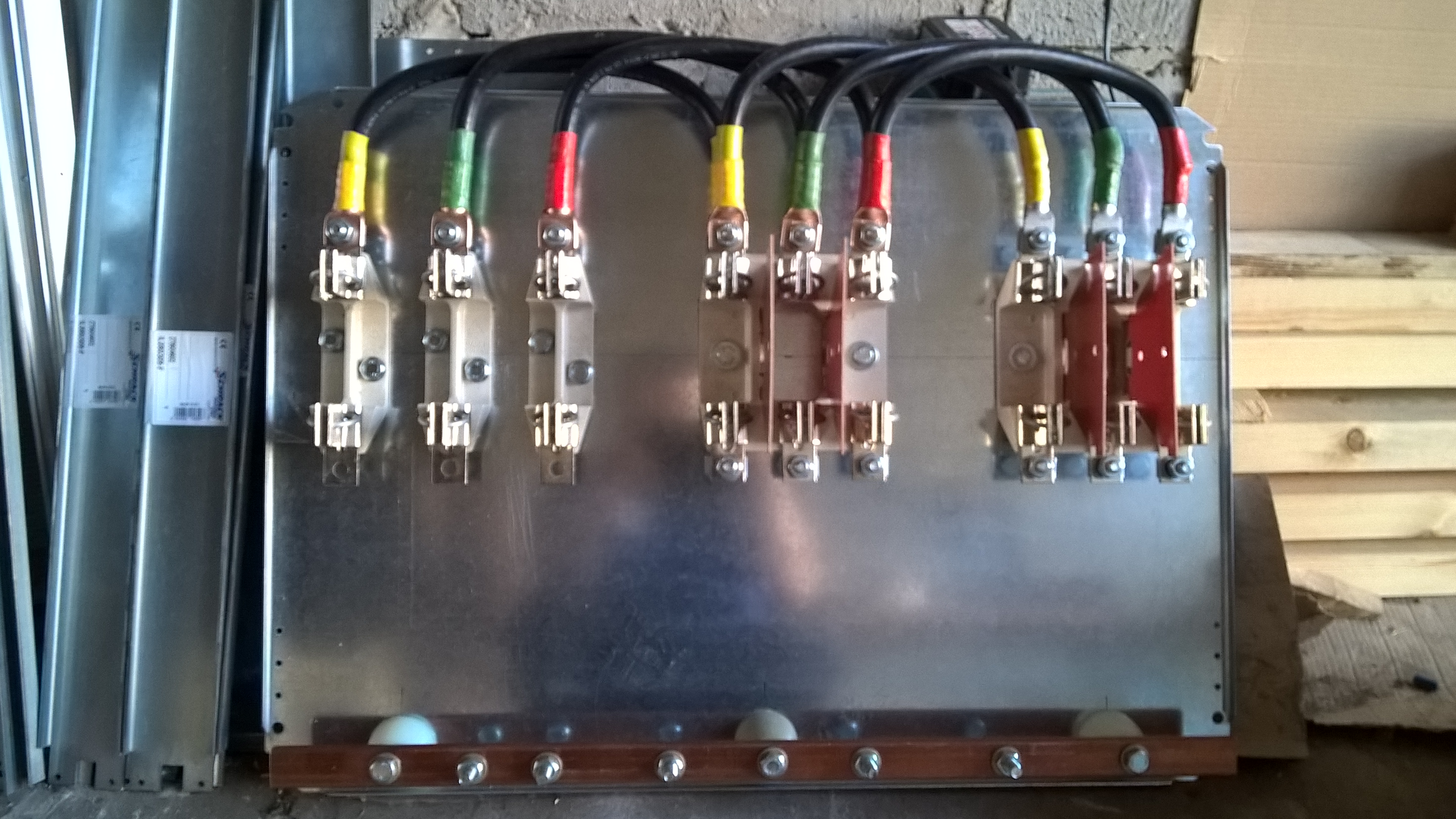 Rozdzielnica elektryczna z podłączonymi przewodami oznaczonymi kolorami: żółty, zielony, czerwony. Widoczne metalowe szyny i izolatory.