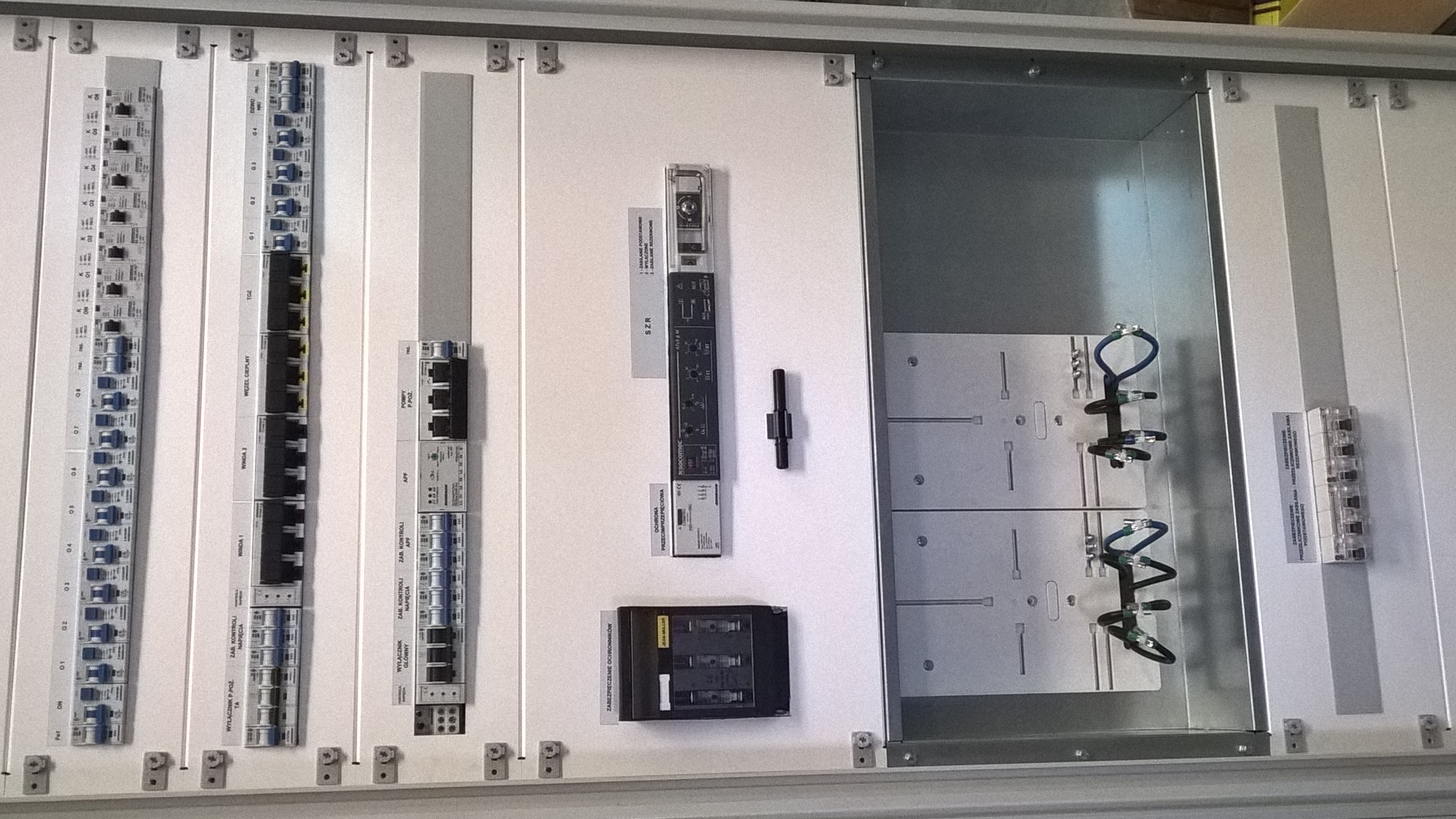 Rozdzielnica elektryczna w trakcie montażu: moduły, kable, zabezpieczenia. Widoczne elementy automatyki i okablowania wewnątrz metalowej obudowy. Praca w toku.