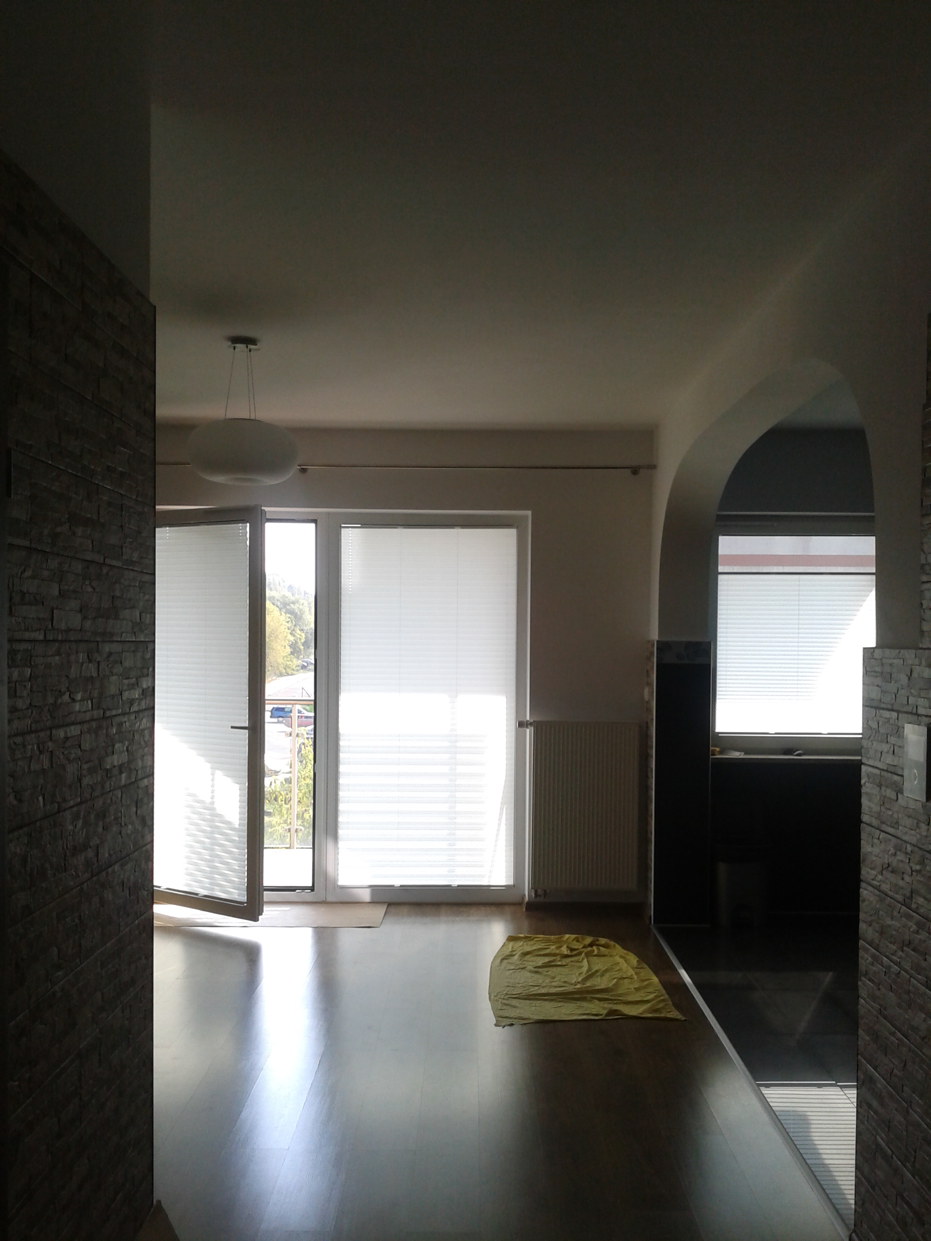 Jasne wnętrze po remoncie: parkiet, okno balkonowe z żaluzjami, dekoracyjna ściana z kamienia. Widok na odnowiony pokój z wykończonymi detalami.