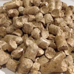 Jasnobrązowy pellet drzewny w dużym skupisku, widoczne detale struktury i nieregularne kształty pojedynczych granulek. Makro, oświetlenie dzienne.