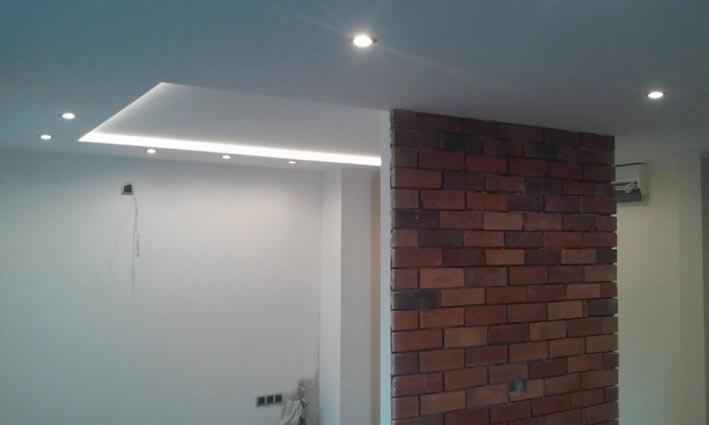 Nowoczesne wykończenie wnętrza z ceglaną ścianą i podwieszanym sufitem z oświetleniem LED. Minimalistyczny design z elementami dekoracyjnymi.