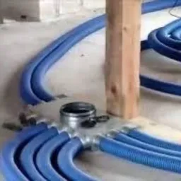 System rozdzielaczowy z niebieskimi przewodami wentylacyjnymi w podłodze, widoczne elementy montażowe, instalacja w Komorowie na etapie układania.