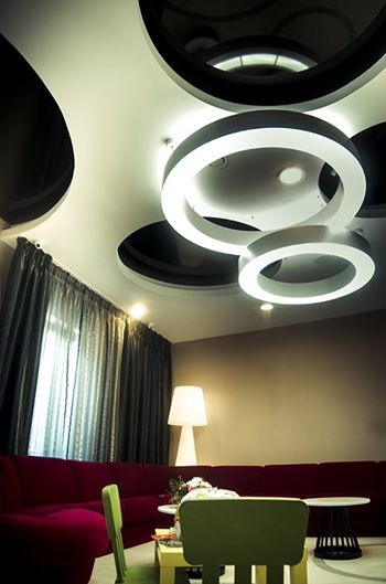 Nowoczesne oświetlenie sufitowe z okrągłymi lampami LED w salonie. Ciemne, dekoracyjne wnęki i szare zasłony w tle. Stylowy wystrój wnętrza.