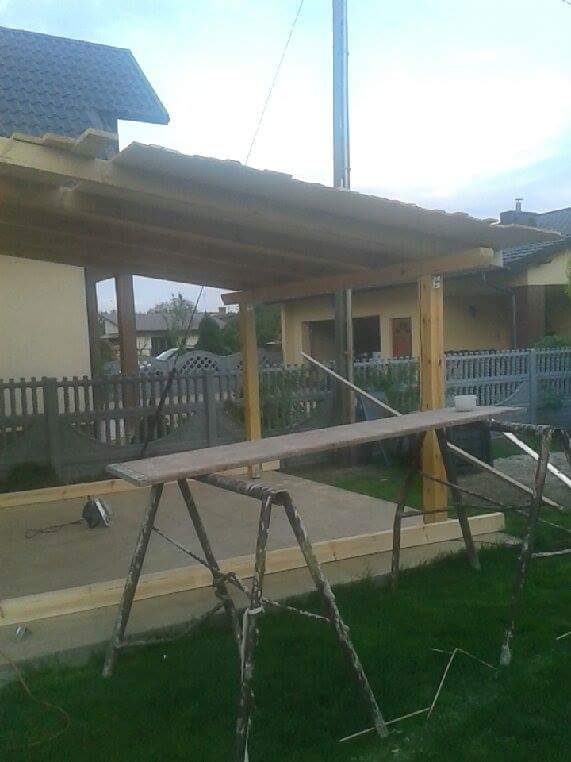 Budowa zadaszenia tarasu w Niskiej zabudowie jednorodzinnej. Widoczne drewniane słupy, konstrukcja dachu i podłoże przygotowane pod wylewkę.