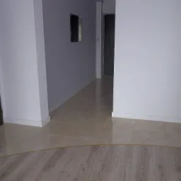 Wykończone wnętrze: Połączenie płytek beżowych i paneli podłogowych w odcieniach drewna, listwy przypodłogowe, jasne ściany. Widok z perspektywy podłogi.