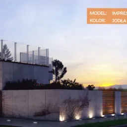 Nowoczesna posesja z aluminiowym ogrodzeniem horyzontalnym w kolorze jodły, betonowym murem z dekoracją w postaci pnącza, podświetlona lampami gruntowymi o ciepłej barwie, widok na dom z tarasem.