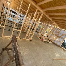 Zielpol 2.0 Dariusz Zieliński - Wnętrze w trakcie budowy domu szkieletowego. Widoczne drewniane ramy ścian, stropu i podłogi. Na podłodze leżą narzędzia, a w tle rusztowania.