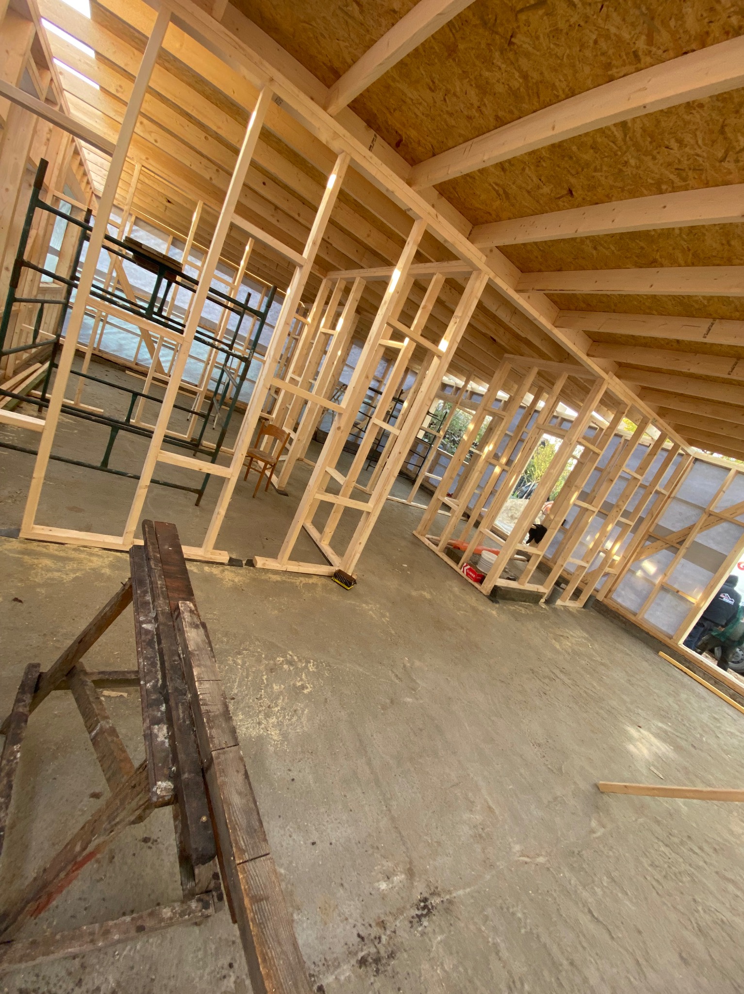 Wnętrze w trakcie budowy domu szkieletowego. Widoczne drewniane ramy ścian, stropu i podłogi. Na podłodze leżą narzędzia, a w tle rusztowania.