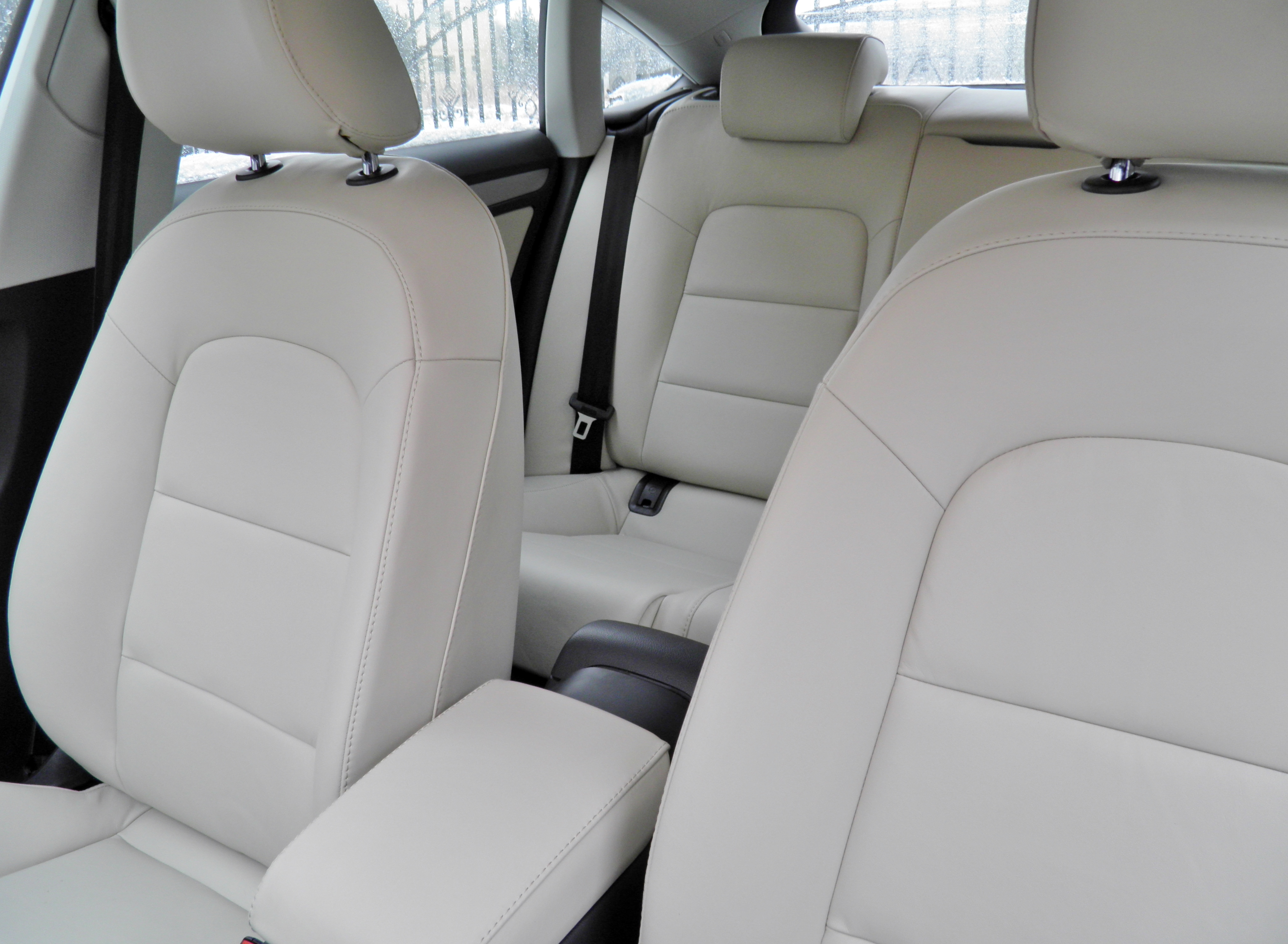 Jasna, skórzana tapicerka samochodowa z widocznymi szwami i zagłówkami. Widok na przednie i tylne siedzenia auta.