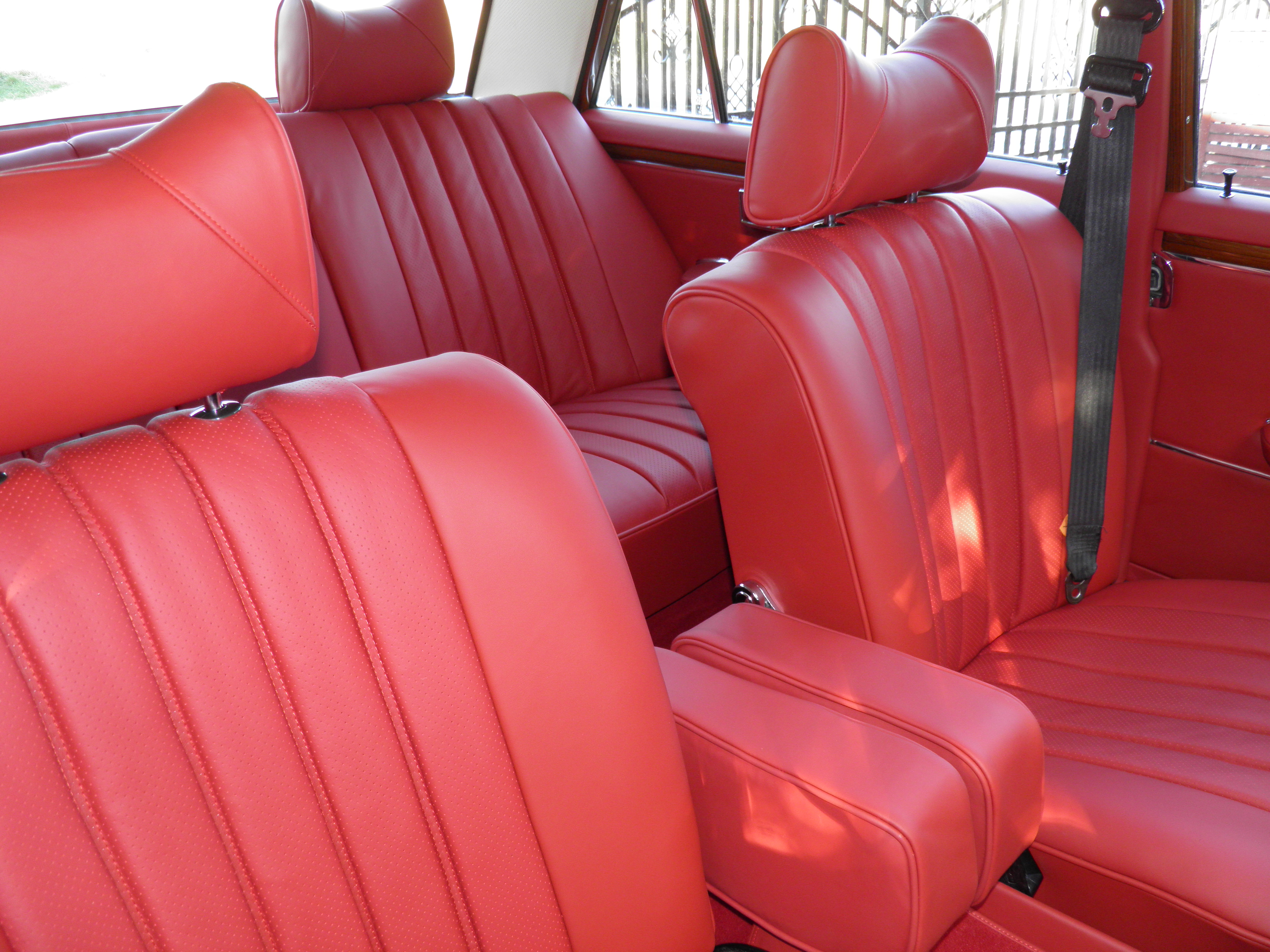 Czerwona, odnowiona tapicerka samochodowa w klasycznym samochodzie. Widoczne fotele z zagłówkami i podłokietnikiem, detale przeszyć.